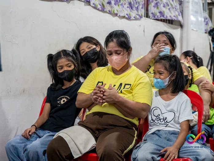 Mothers in yellow shirts sit with their daughters, listening.