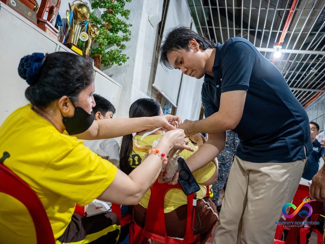 A Foundation staff member leans in to assist a mother and child seated on red chairs.